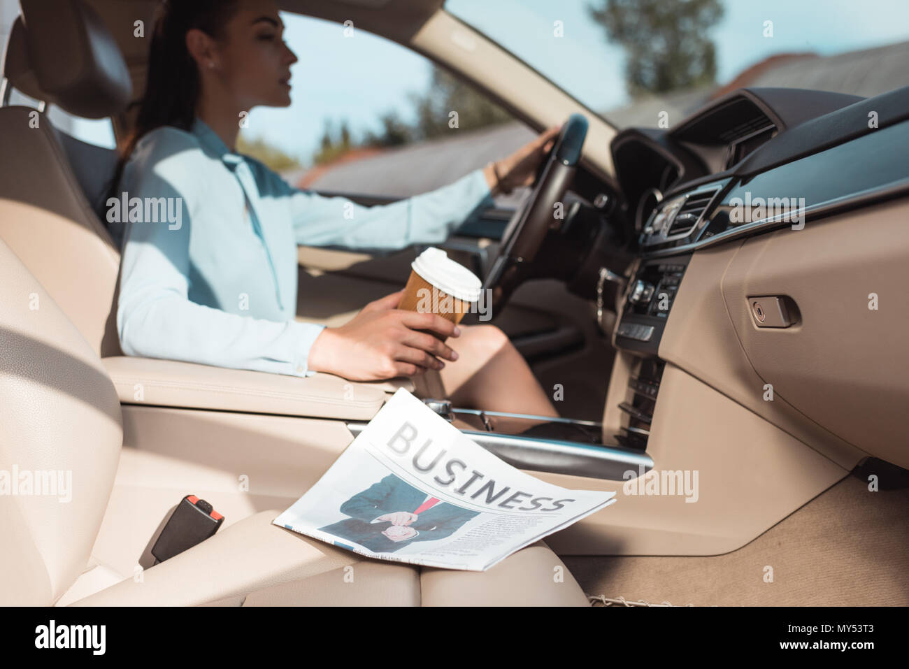 Giovane donna alla guida di una vettura con business giornale giacente nel sedile anteriore Foto Stock