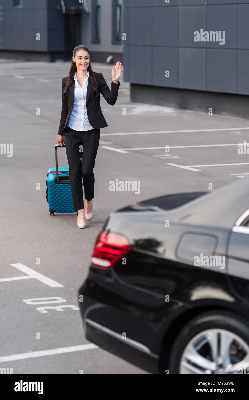 Giovane donna di pant suit camminando verso il passeggero con auto valigia Foto Stock