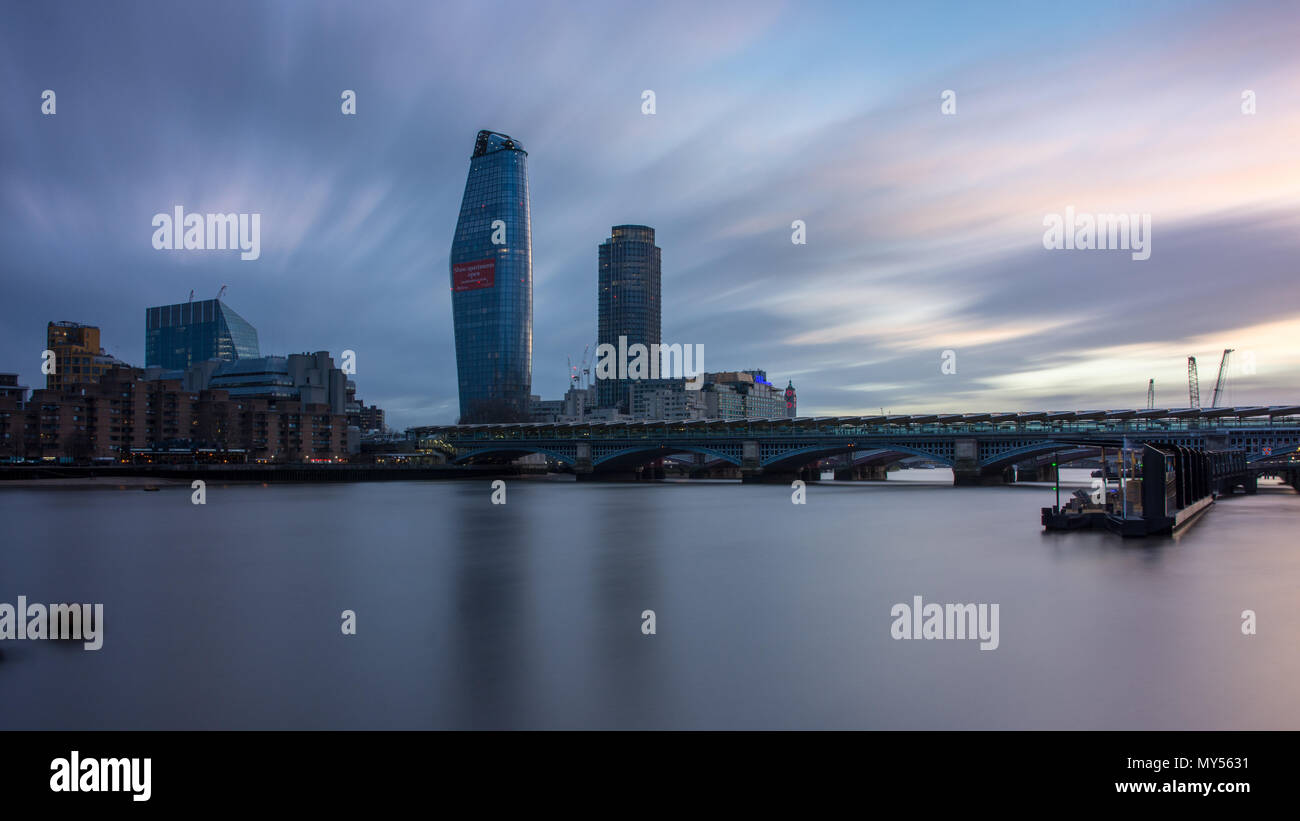 London, England, Regno Unito - 3 Aprile 2018: Il fiume Tamigi scorre sotto il Blackfriars stazione ferroviaria, con la sponda sud skyline dietro al tramonto. Foto Stock