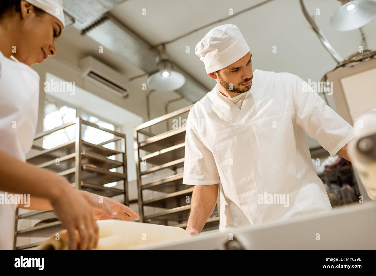 Giovani fiduciosi bakers lavora con impasto industriale rullo alla fabbricazione di cottura Foto Stock