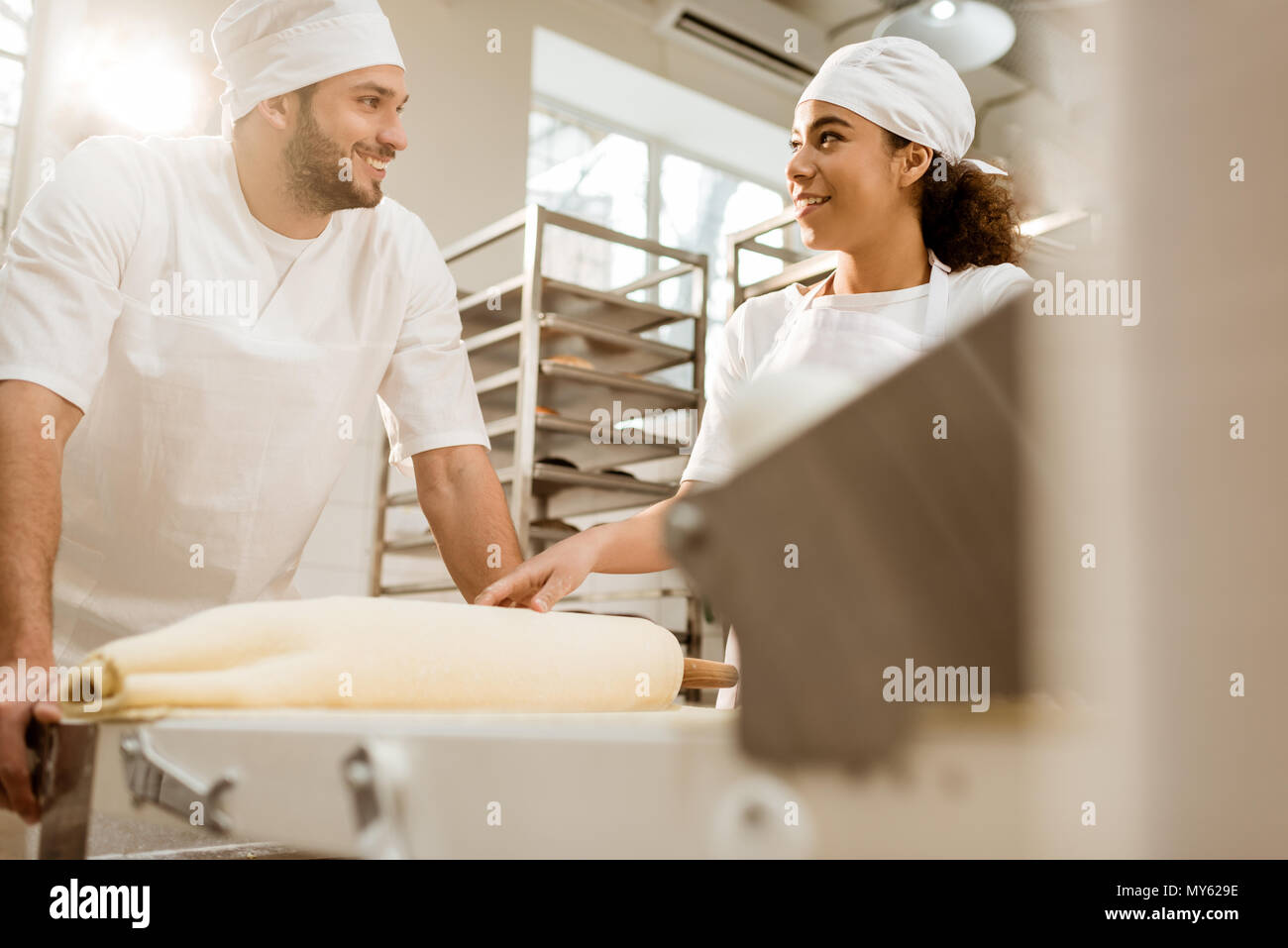 Felice giovani fornai lavora con impasto industriale rullo alla fabbricazione di cottura Foto Stock