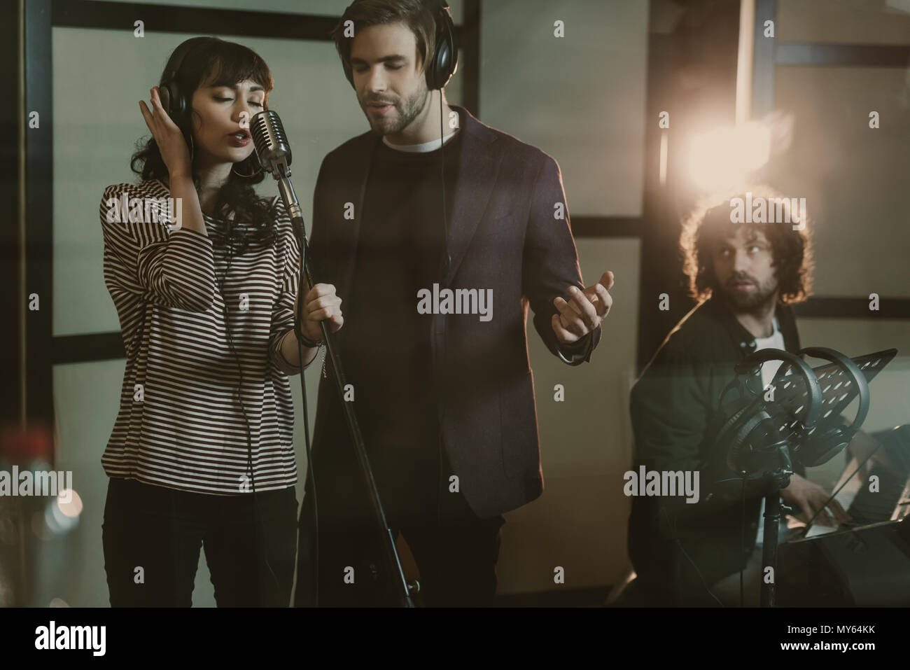 Giovani cantanti di eseguire la canzone mentre l uomo suonando piano sullo sfondo Foto Stock