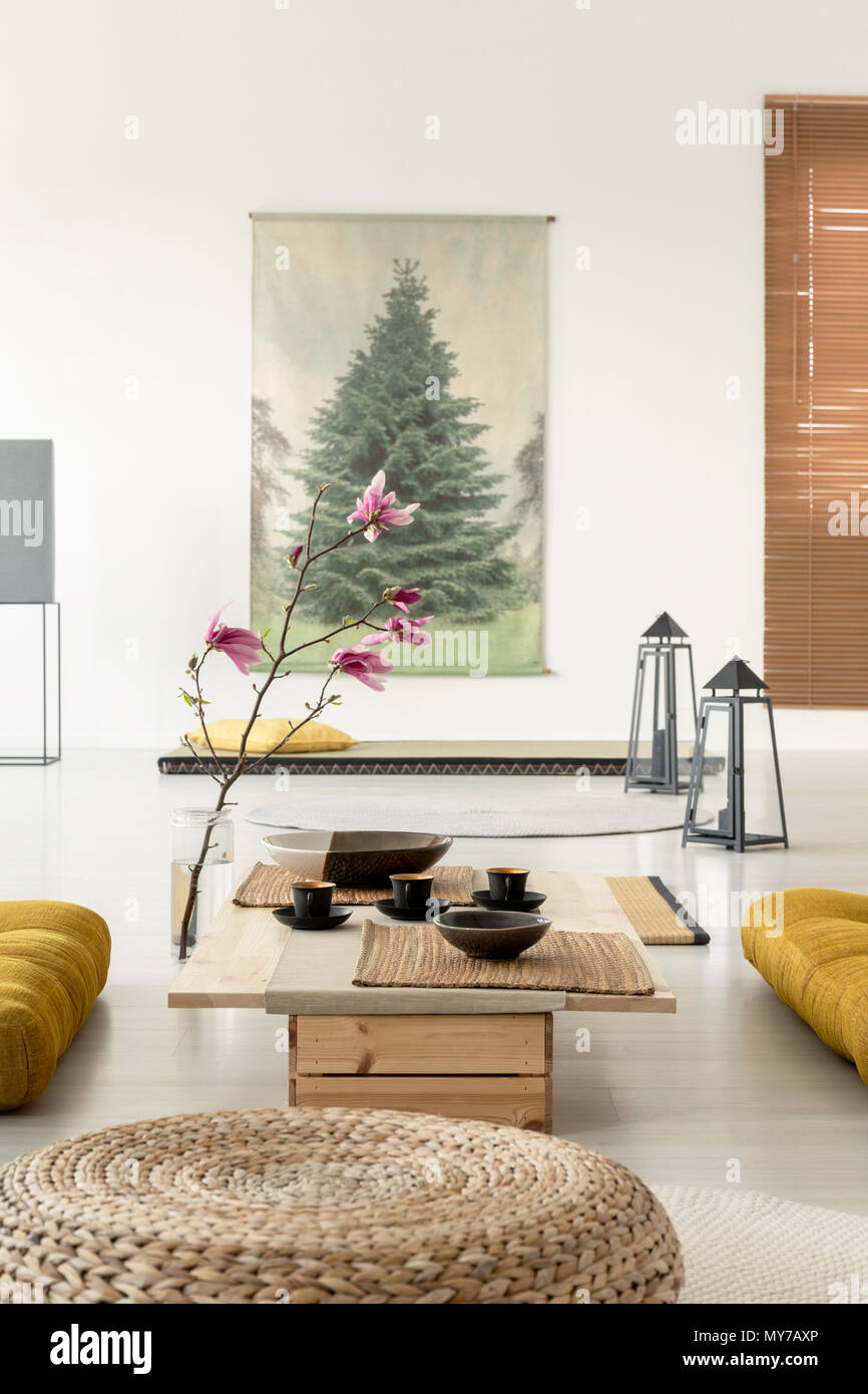 Close-up di un pouf in un salotto interno con un tavolo da caffè, la fioritura dei ciliegi, lampade sul pavimento e un poster di albero Foto Stock