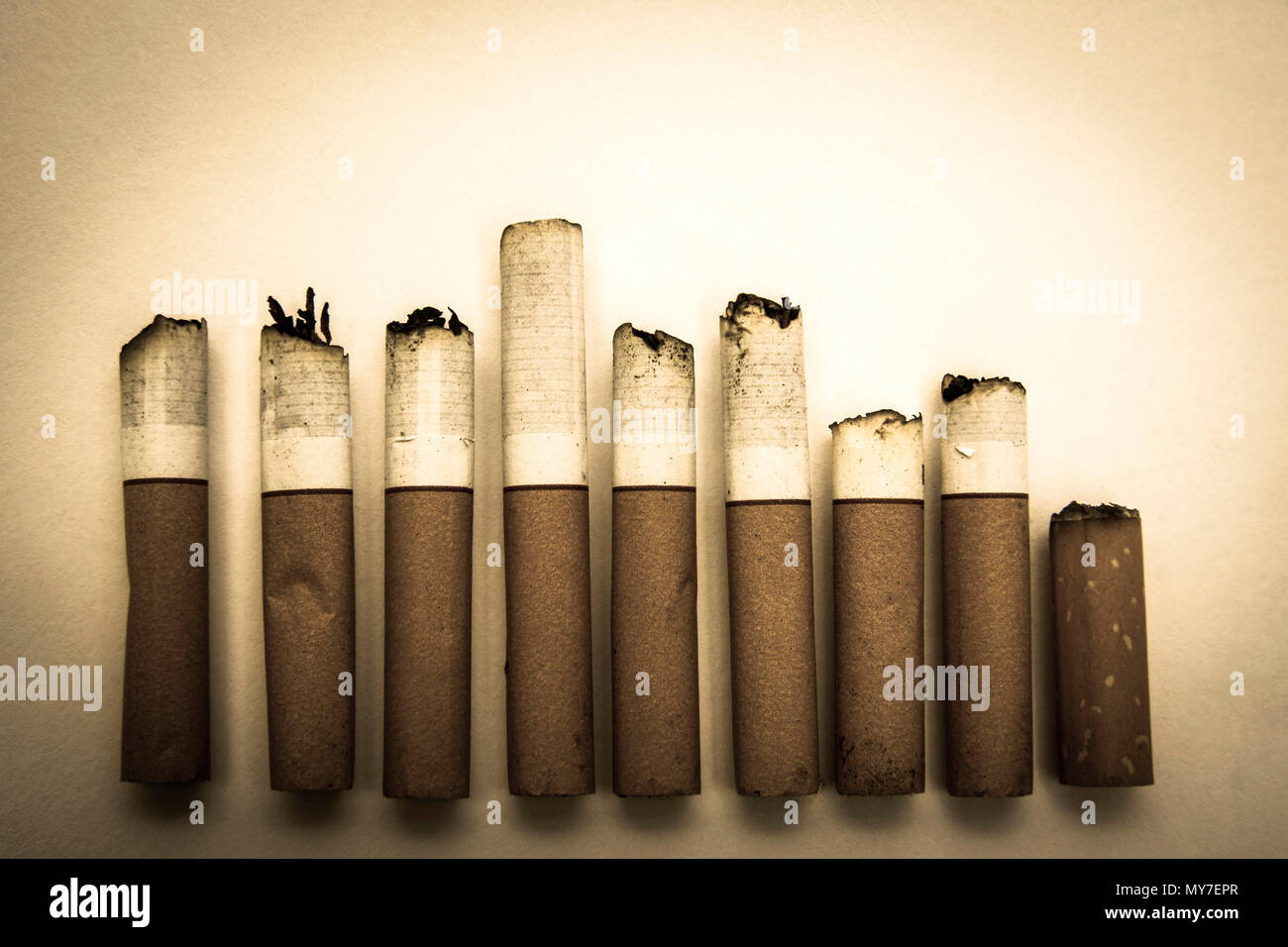 Sigarette impilate disposte su uno sfondo semplice con punte bruciate Foto Stock