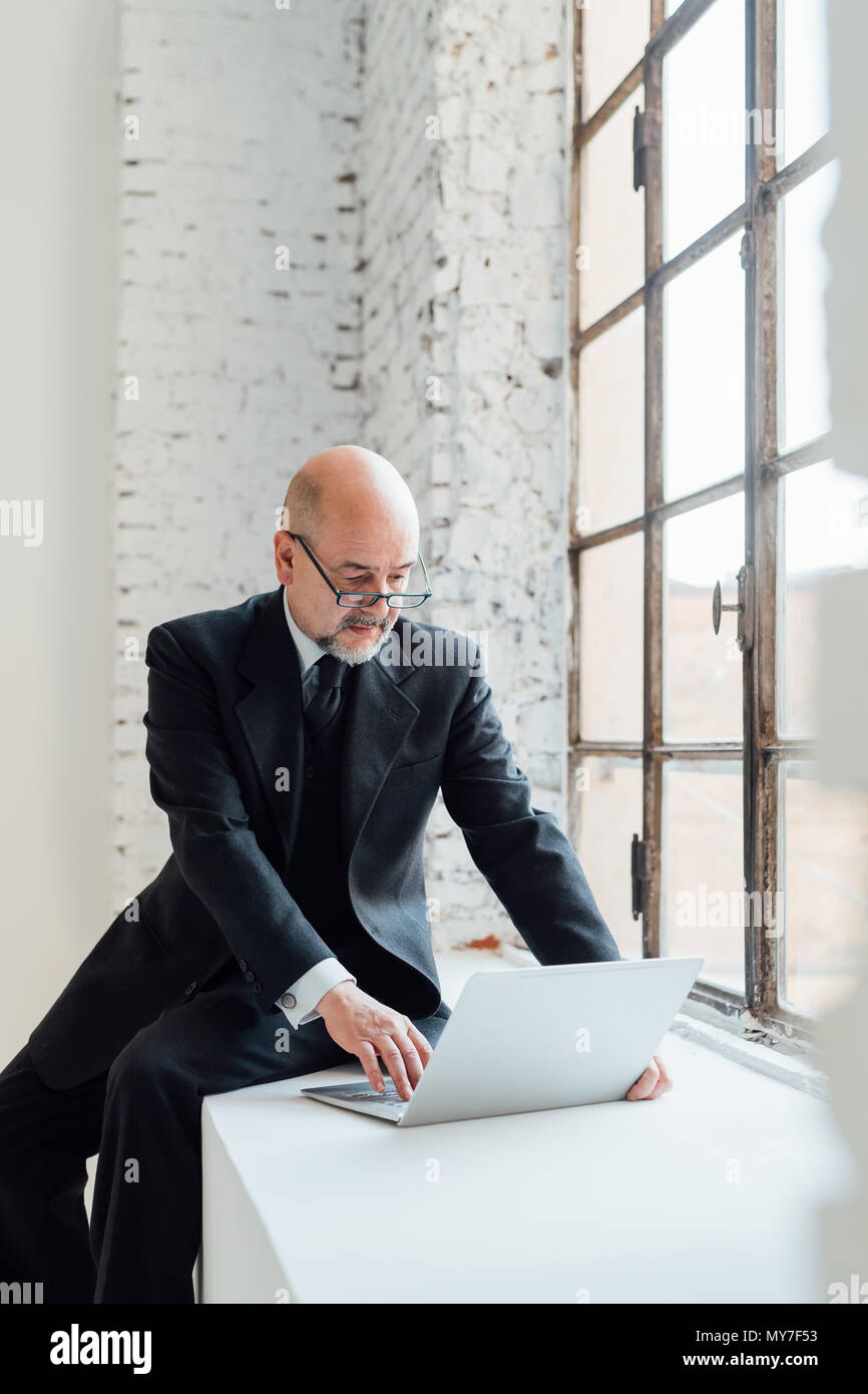 Imprenditore seduto sul davanzale utilizzando laptop Foto Stock