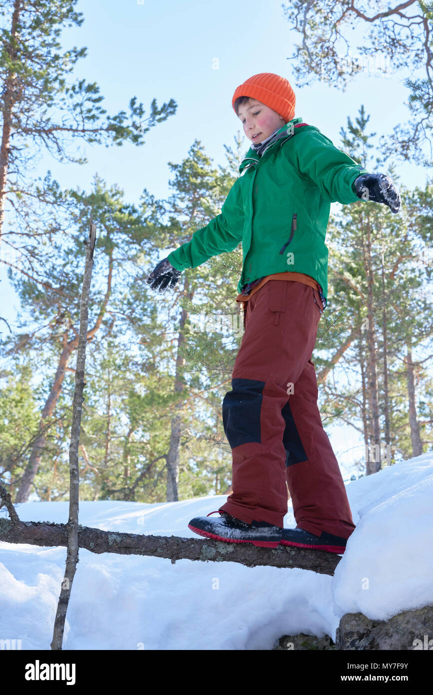 Ragazzo giovane camminare sul ramo di albero in coperta di neve, il paesaggio rurale e a basso angolo di visione Foto Stock