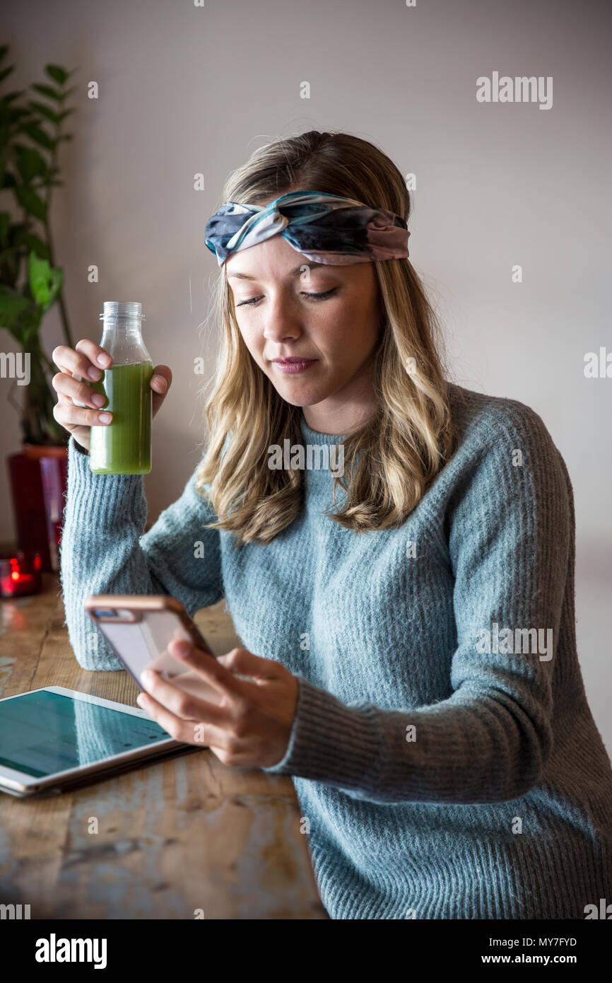 Giovane donna con un succo vegetale guardando smartphone a cafe sedile finestra Foto Stock