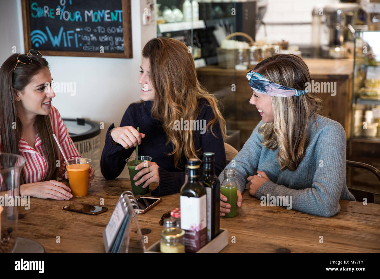 Tre giovani amici di sesso femminile con un succo vegetale chiacchierando in cafe Foto Stock