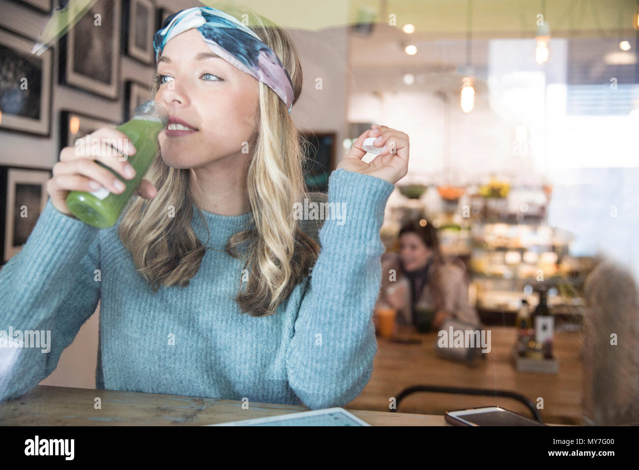 Giovane donna di bere succo di verdura al cafe finestrino Foto Stock