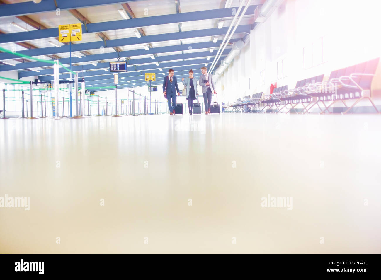 Imprenditrice e gli uomini a piedi attraverso l'aeroporto con la valigia con ruote Foto Stock