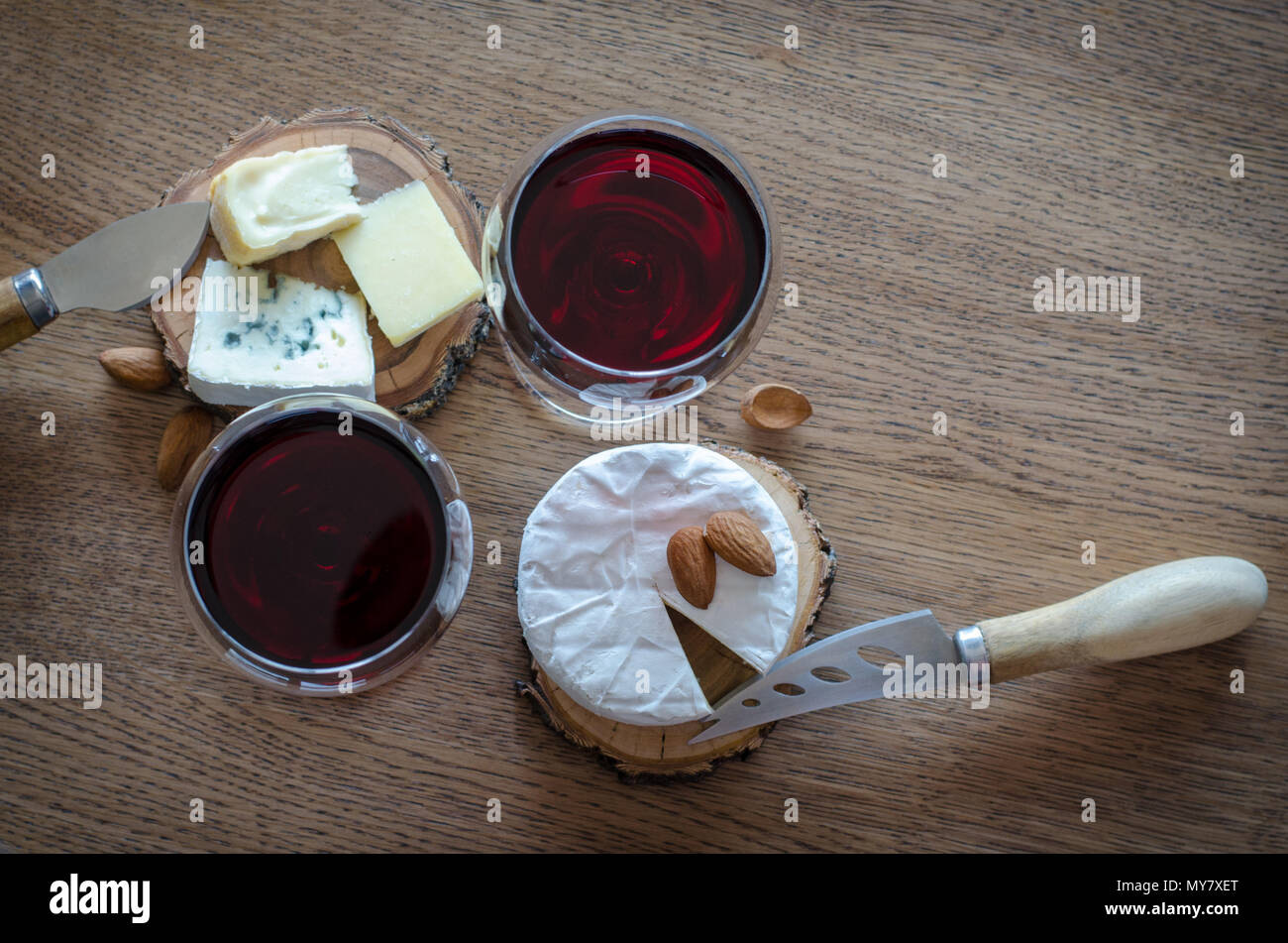 2 bicchiere di vino rosso con pochi pezzi di formaggio e i coltelli a sfondo di legno. vista superiore Foto Stock