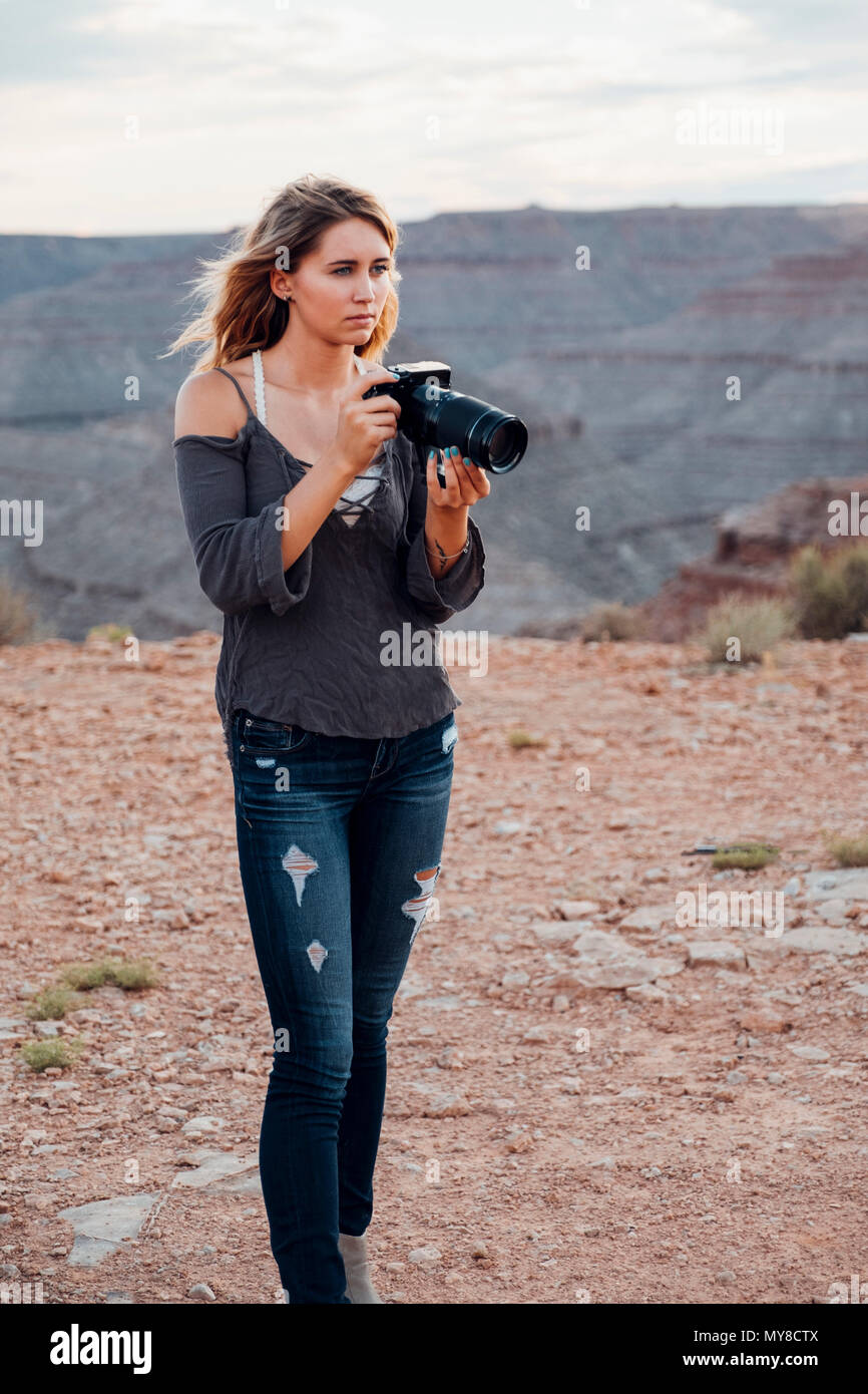 Giovane donna all'aperto, tenendo la fotocamera reflex, fotografando dintorni, Mexican Hat, Utah, Stati Uniti d'America Foto Stock