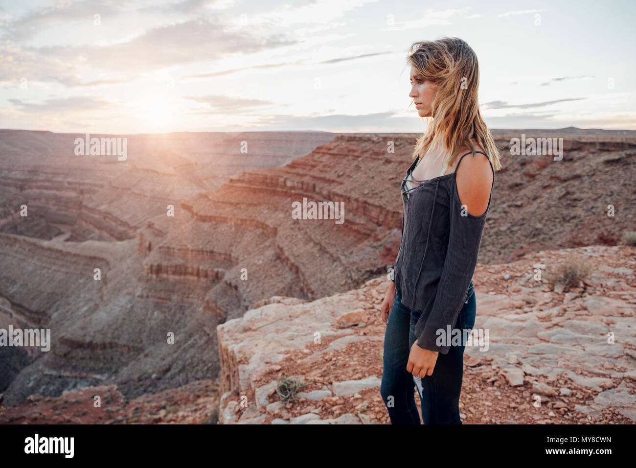 Giovane donna in impostazione remota, in piedi sul bordo di scogliera, guardando a vista, vista posteriore, Mexican Hat, Utah, Stati Uniti d'America Foto Stock