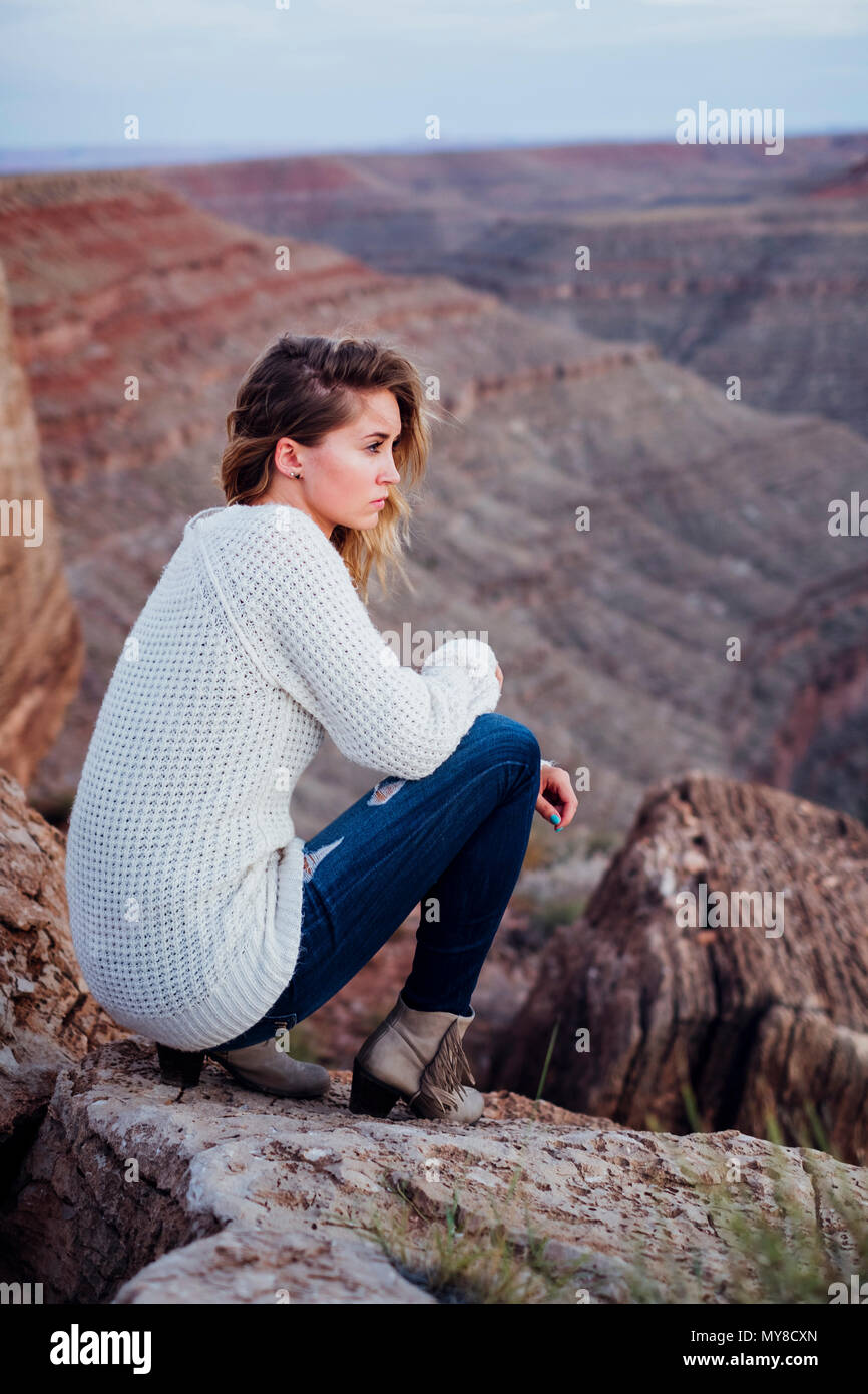 Giovane donna in impostazione remota, seduti sulle rocce, guardando a vista, Mexican Hat, Utah, Stati Uniti d'America Foto Stock