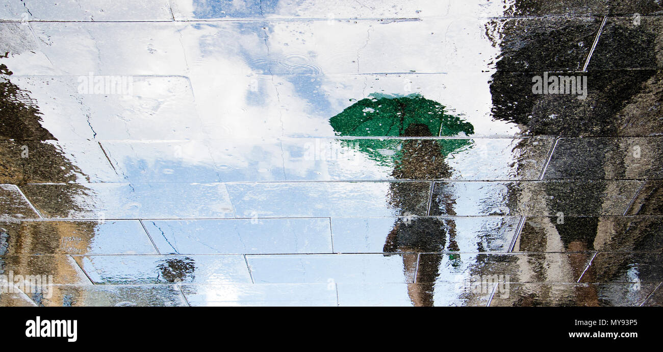 Sfocata riflessione ombra sagome delle persone che camminano in una piovosa strada pedonale in estate Foto Stock
