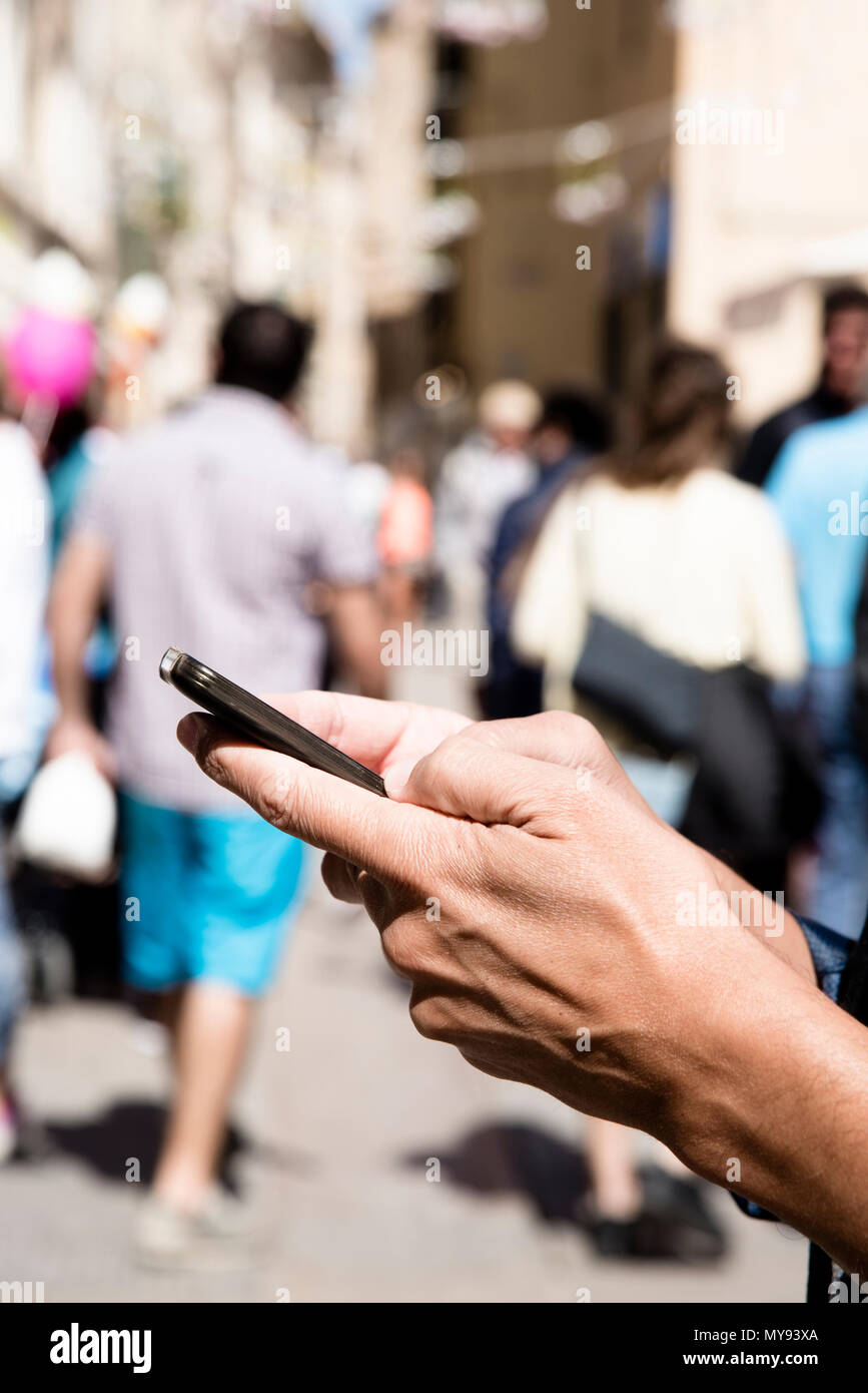 Primo piano di un giovane uomo caucasico utilizzando uno smartphone in una affollata strada pedonale Foto Stock