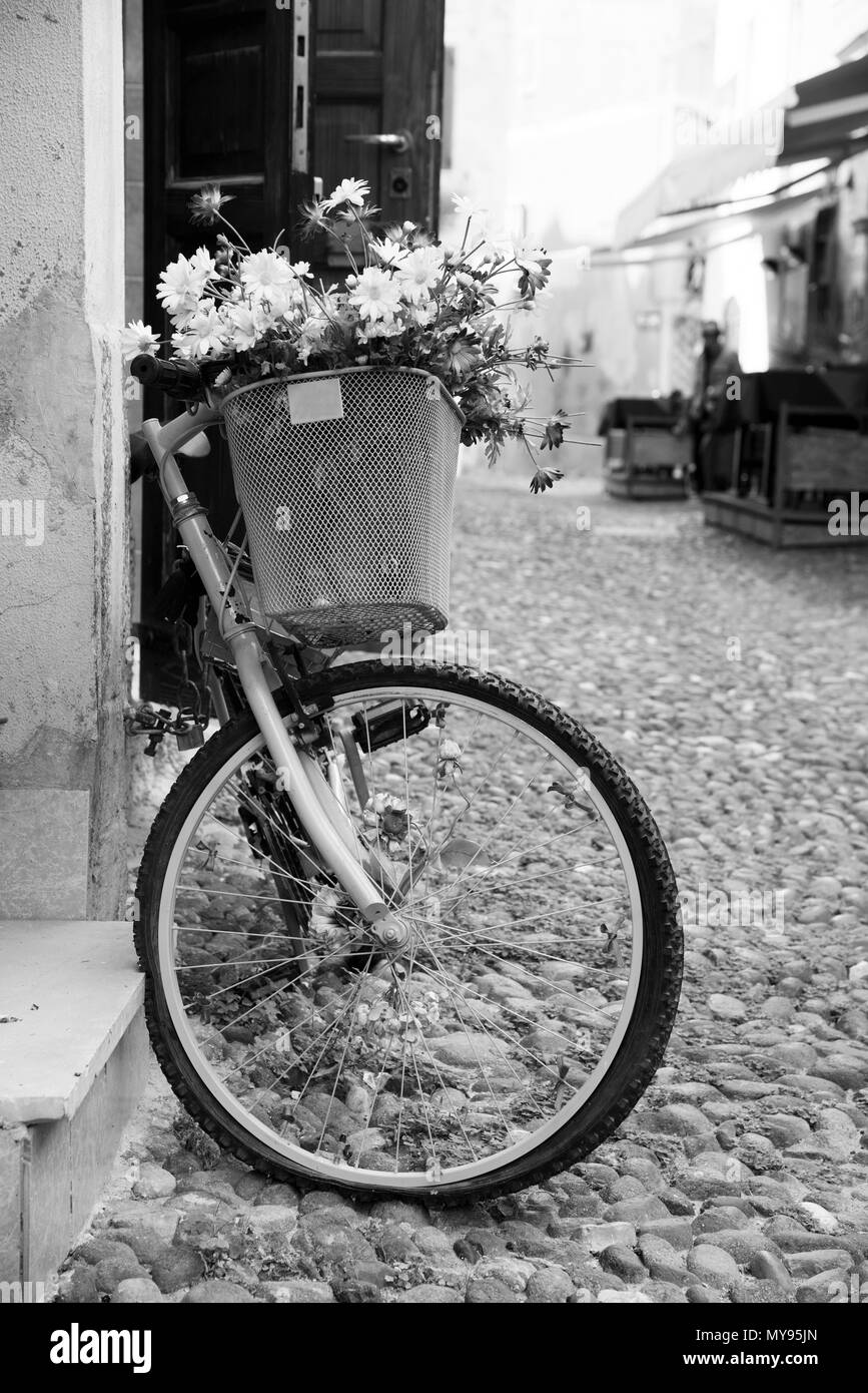 Una vista di una strada pedonale nel centro storico di Alghero, Sardegna, Italia, con una vecchia bicicletta parcheggiata in una parete in primo piano in bianco e nero Foto Stock