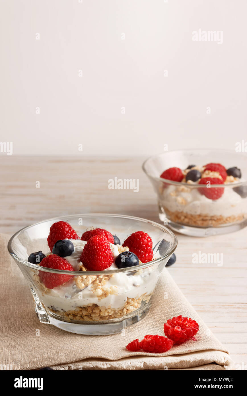 Lamponi Mirtilli, cereali e yogurt in una ciotola di vetro su un letto di sacco e di assicelle di legno. Una sana colazione per una vita sana. L'immagine verticale. Foto Stock