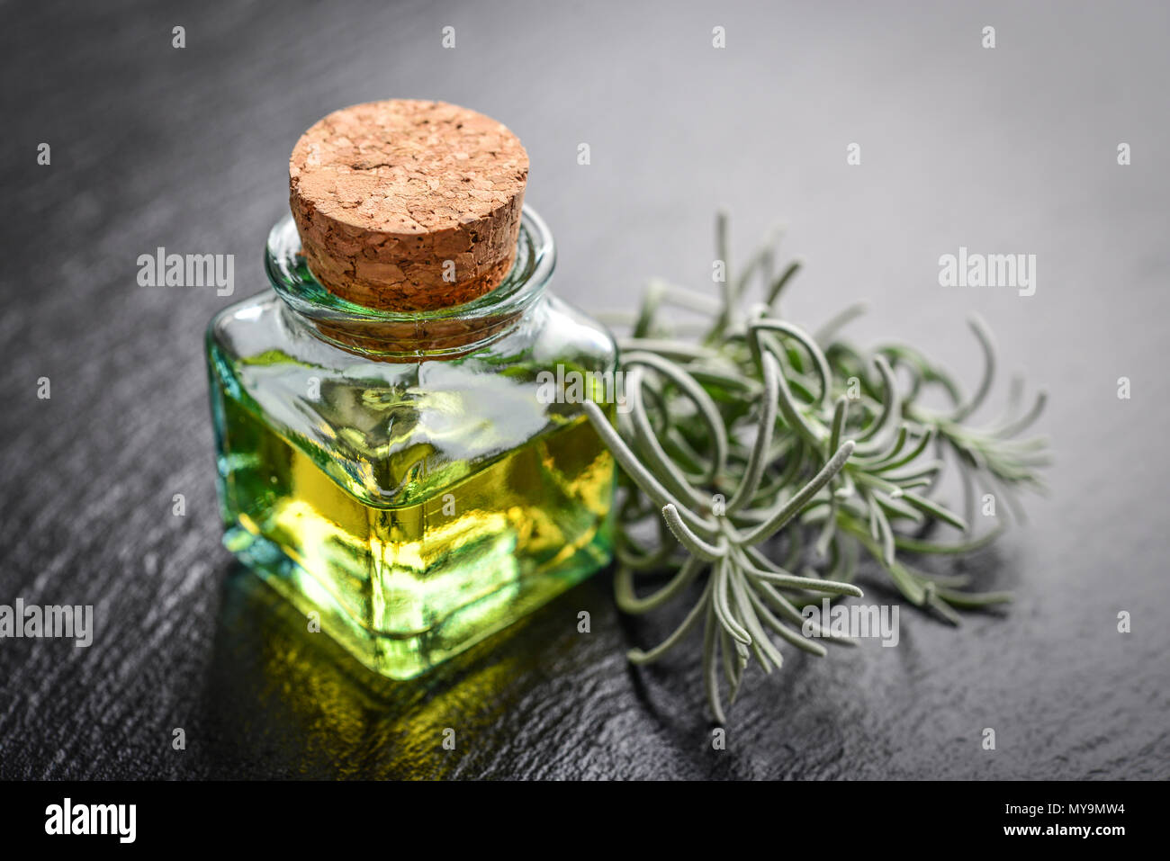 L'olio essenziale di lavanda in una bottiglia di vetro con tappo di sughero e fresche erbe lavanda nero su sfondo di ardesia Foto Stock