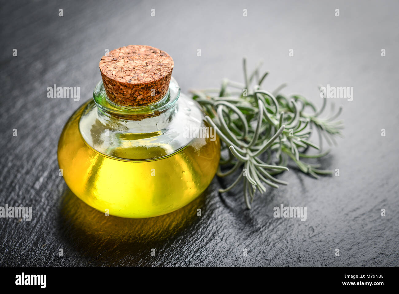 L'olio essenziale di lavanda in una bottiglia di vetro con tappo di sughero e fresche erbe lavanda nero su sfondo di ardesia Foto Stock