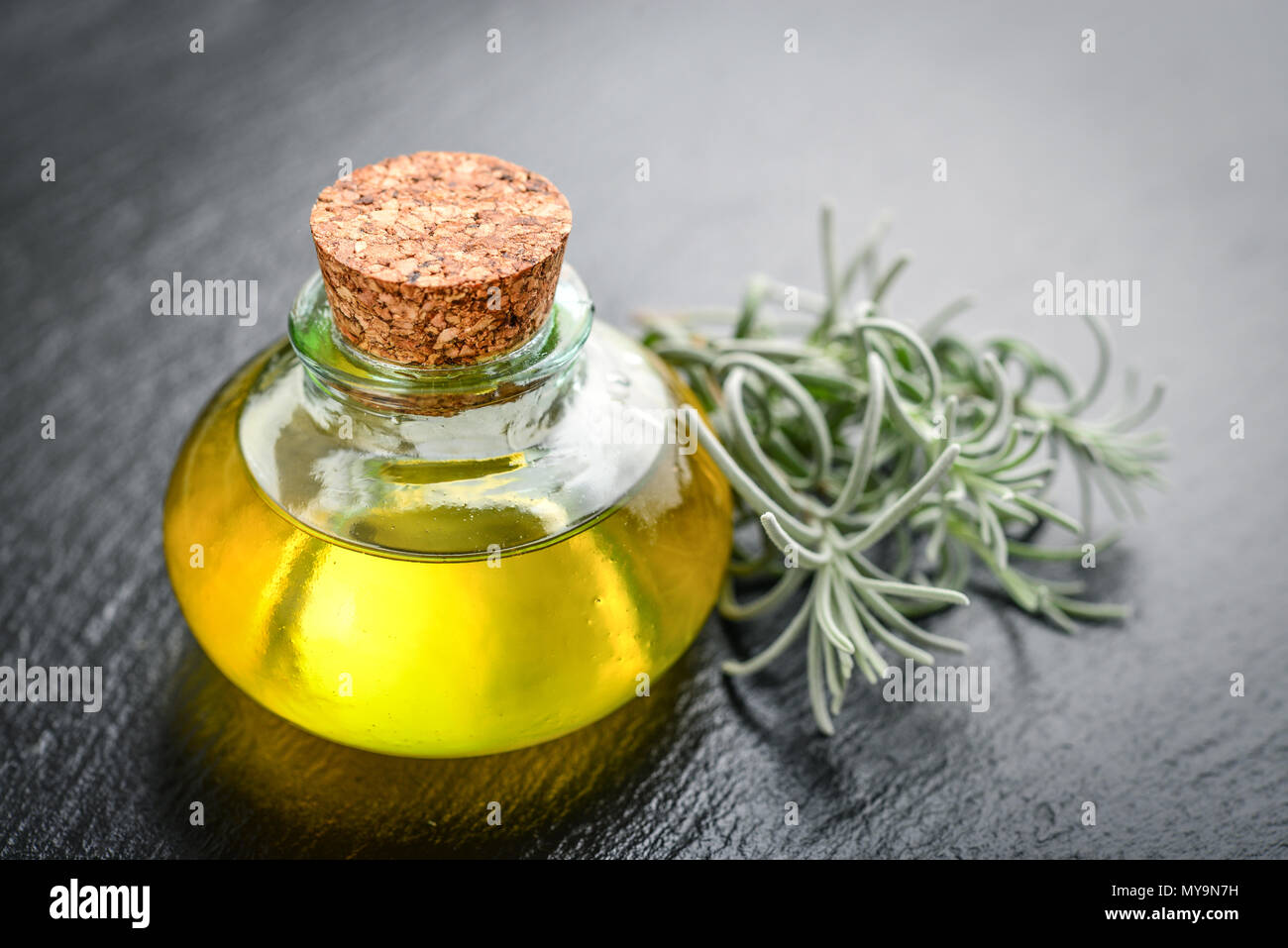 L'olio essenziale di lavanda in una bottiglia di vetro con tappo di sughero e fresche erbe lavanda nero su sfondo di ardesia Foto Stock