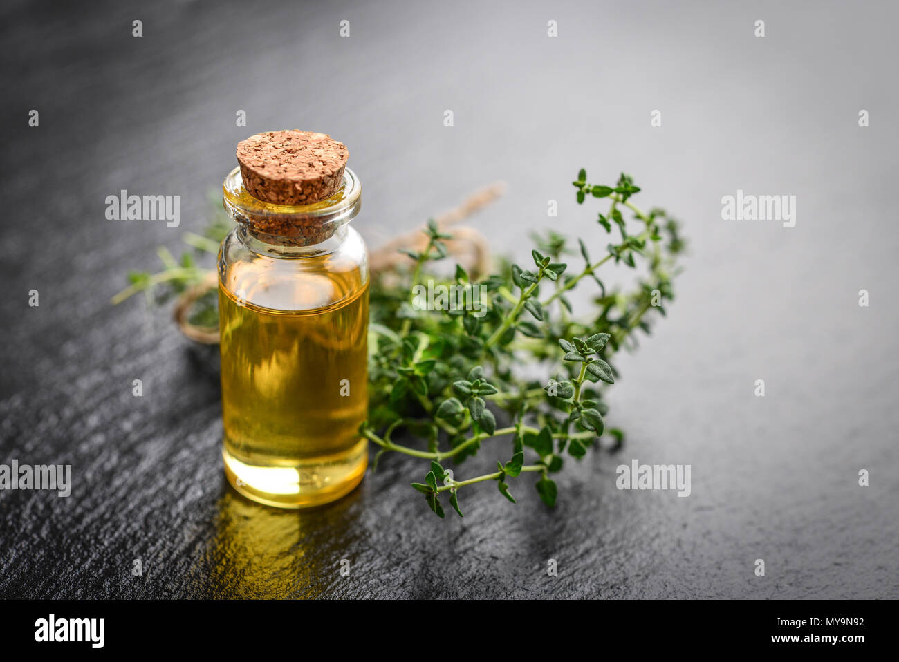 Olio essenziale di timo in un flacone di vetro con tappo di sughero e di timo fresco cantato sul nero ardesia sfondo Foto Stock