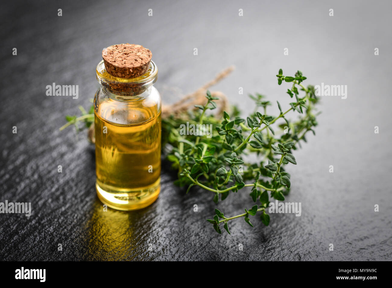 Olio essenziale di timo in un flacone di vetro con tappo di sughero e di timo fresco cantato sul nero ardesia sfondo Foto Stock