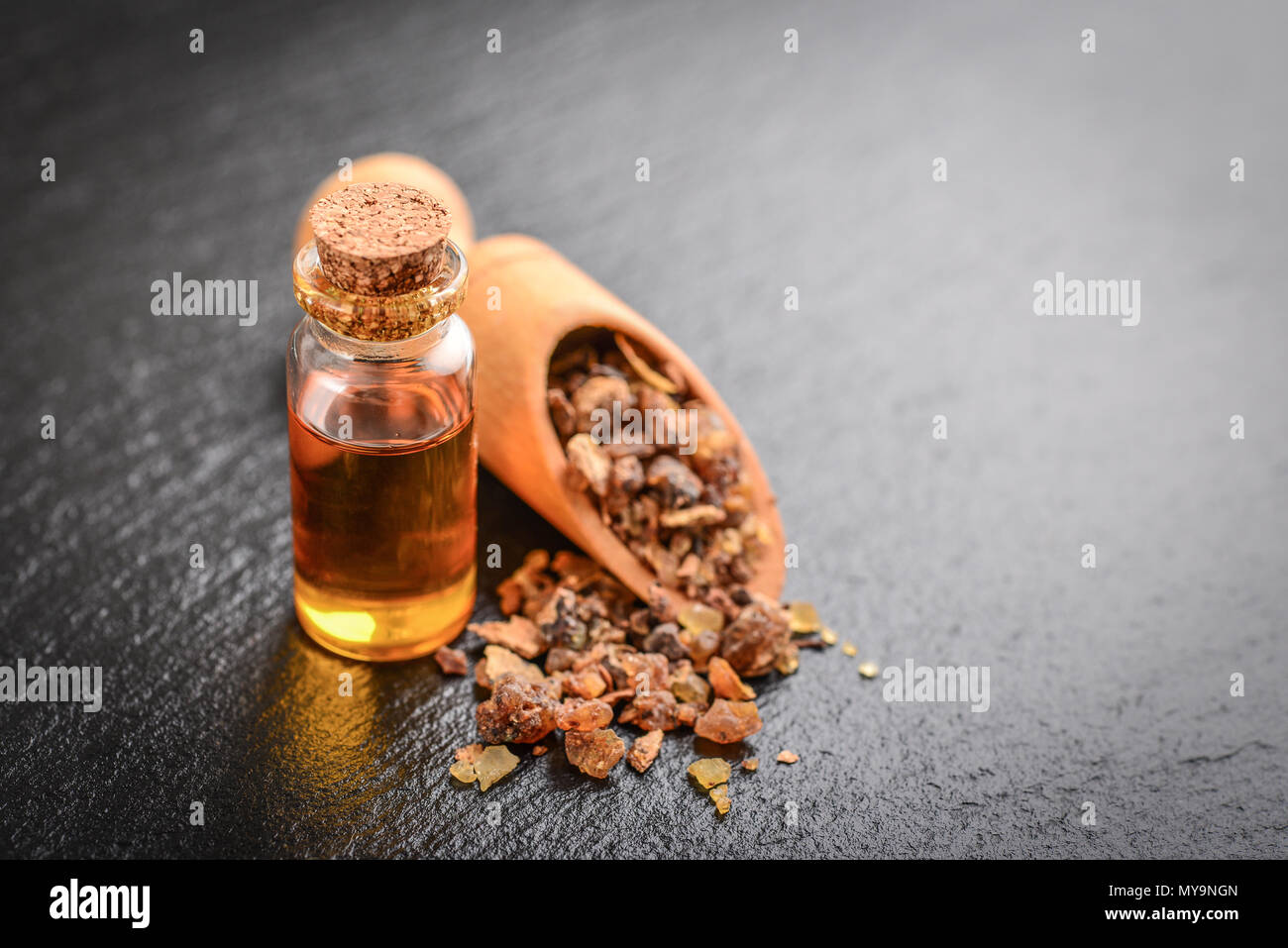 Una bottiglia di mirra olio essenziale di mirra resina su un nero ardesia sfondo Foto Stock