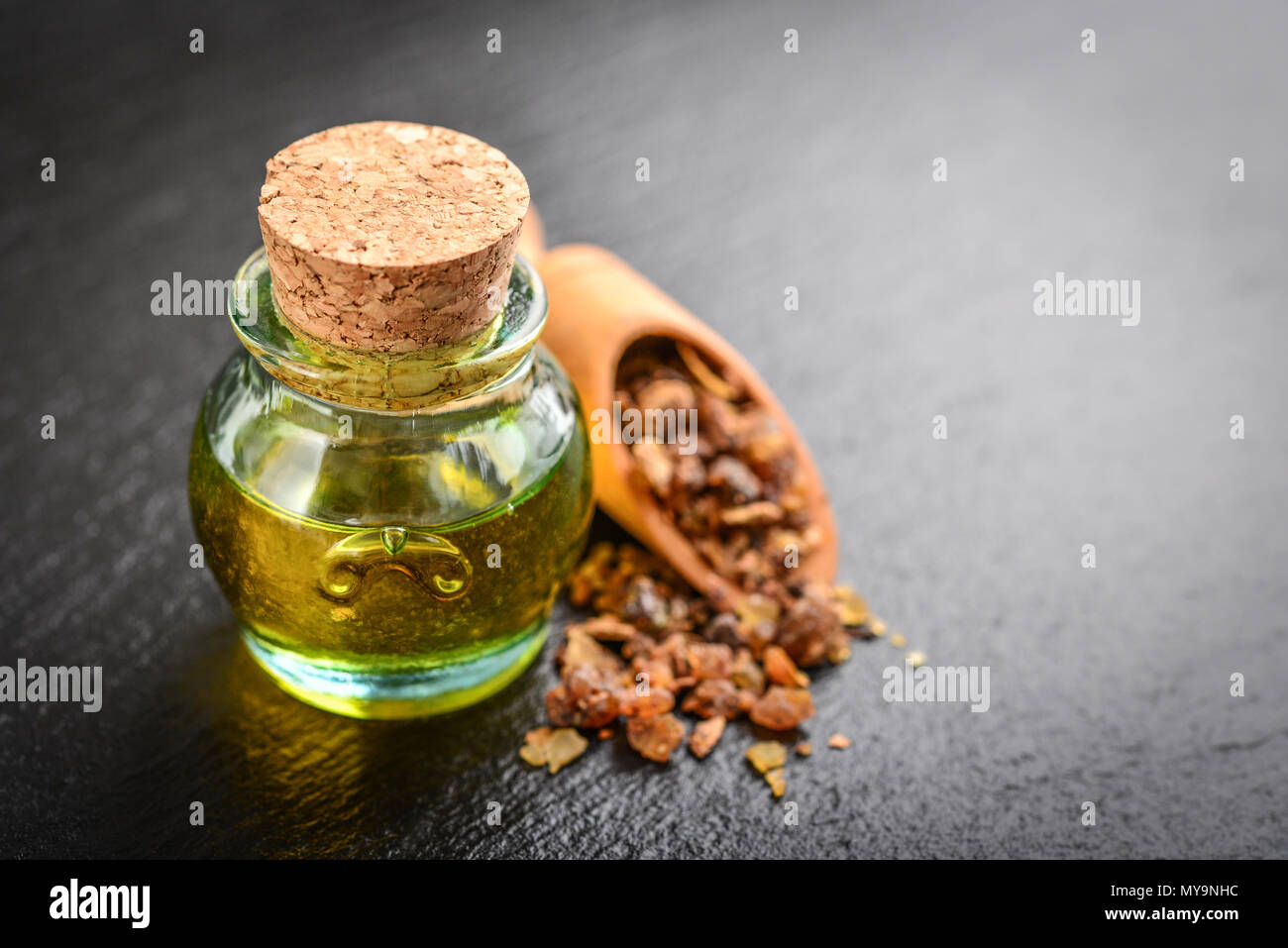 Una bottiglia di mirra olio essenziale di mirra resina su un nero ardesia sfondo Foto Stock