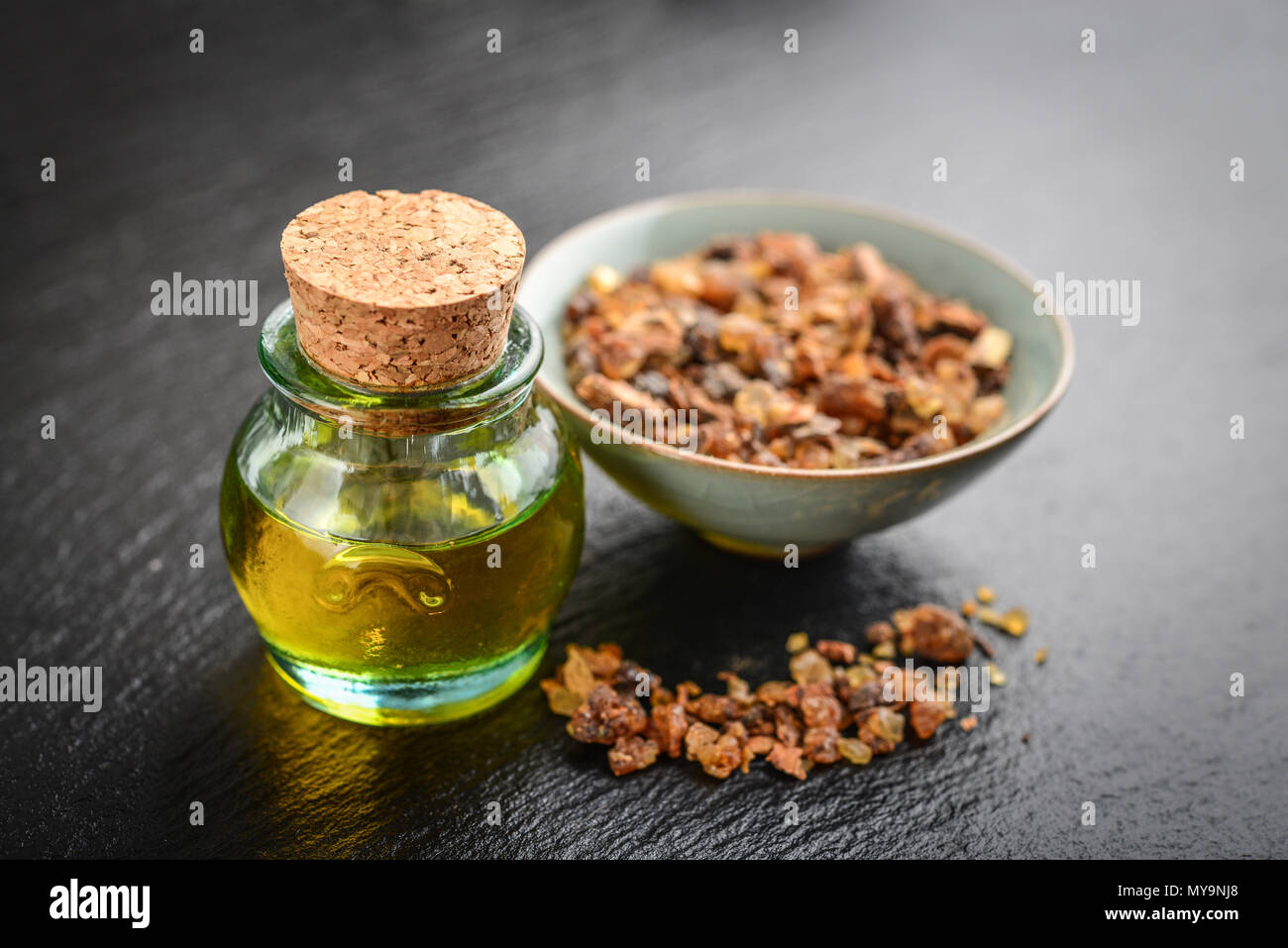 Una bottiglia di mirra olio essenziale di mirra resina su un nero ardesia sfondo Foto Stock
