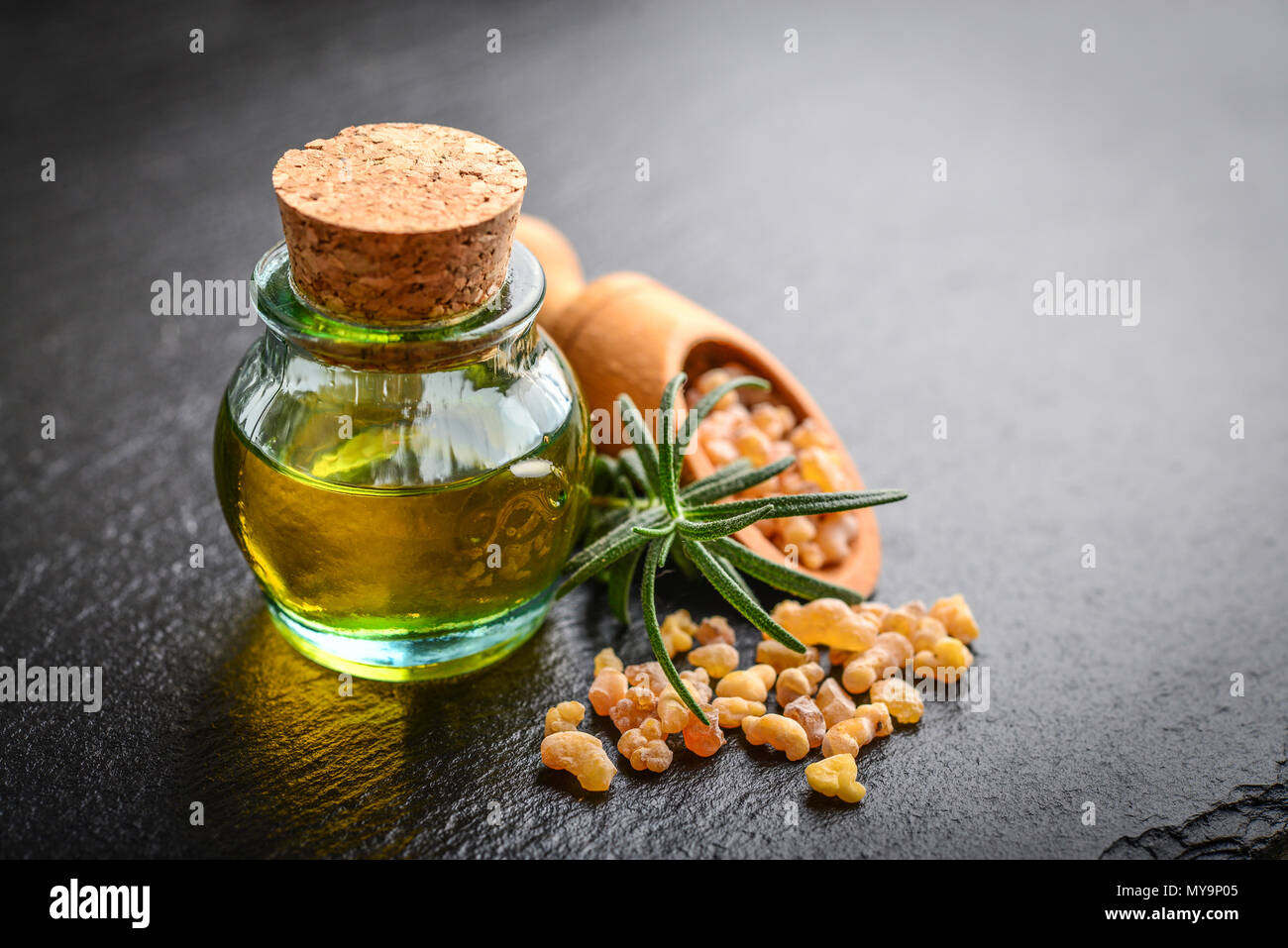 Una bottiglia di incenso olio essenziale di incenso di cristalli di resina sul nero ardesia sfondo Foto Stock