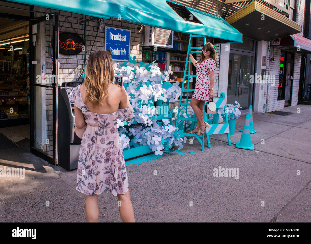 Giovane donna di fotografare il suo amico stando in piedi sulla scala, al di fuori del negozio, entrambe le donne indossano motivi floreali abiti, New York City, Stati Uniti d'America Foto Stock