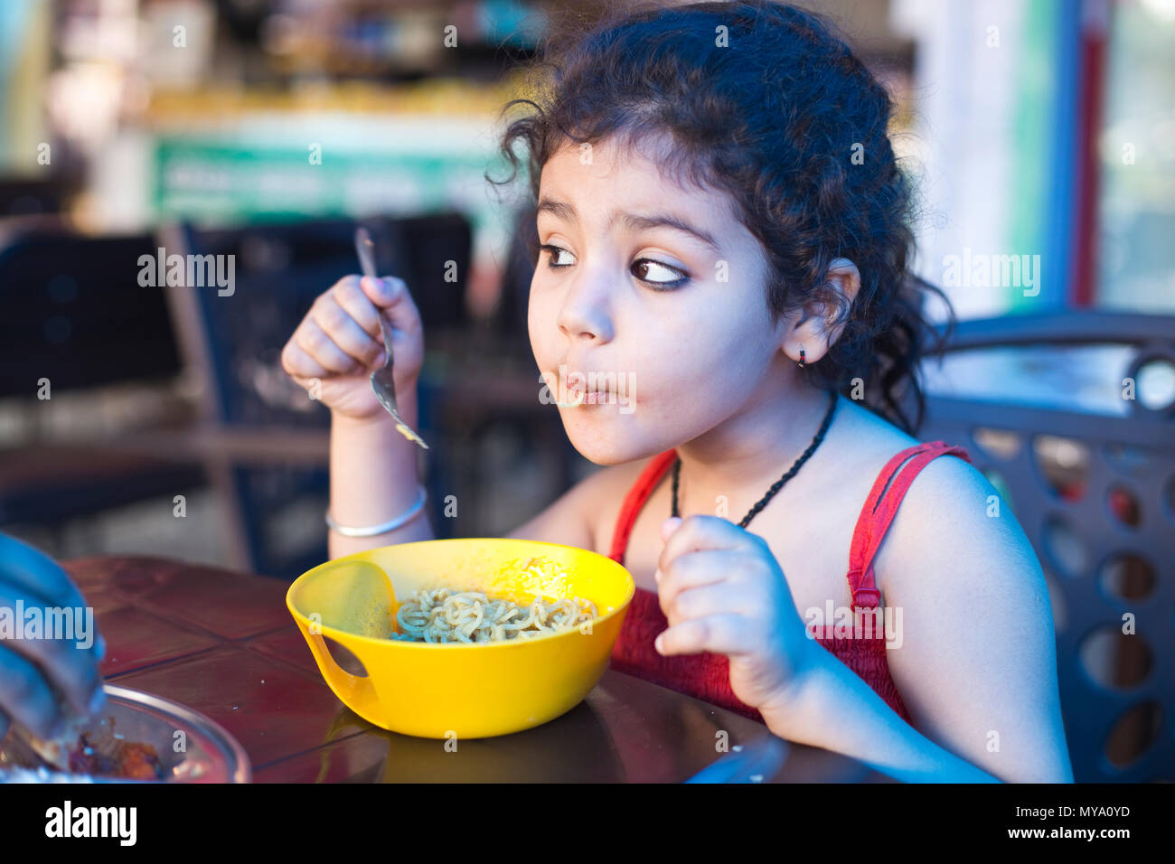 Un indiano bambina mangiare tagliatelle al ristorante Foto Stock