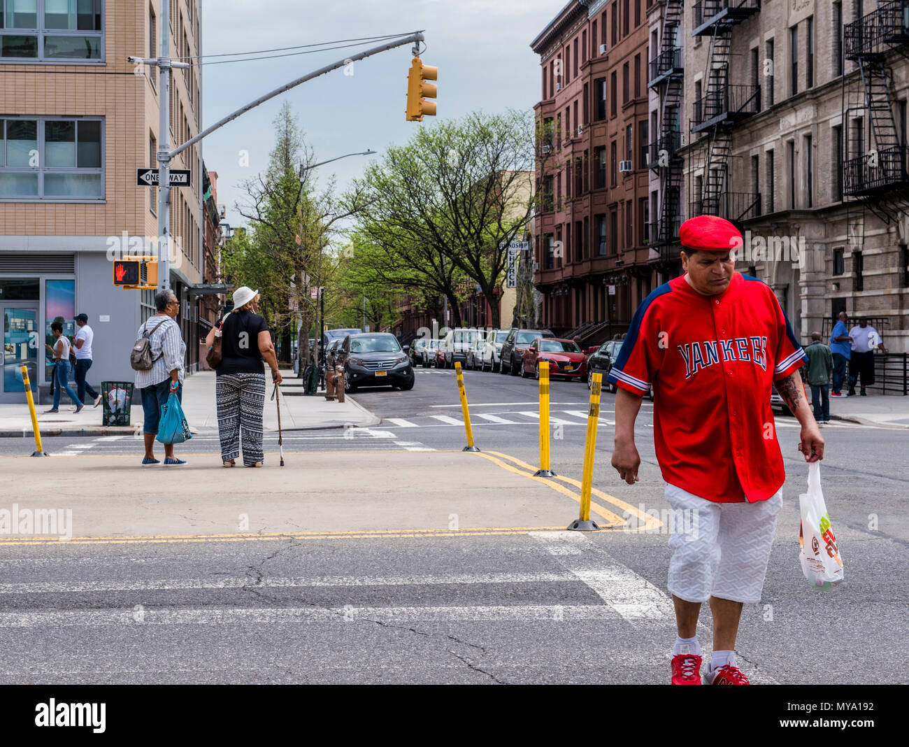 Uomo che indossa Yankees superiore e tappo piatto, attraversando la strada, camminando verso la telecamera Harlem, New York City, Stati Uniti d'America Foto Stock