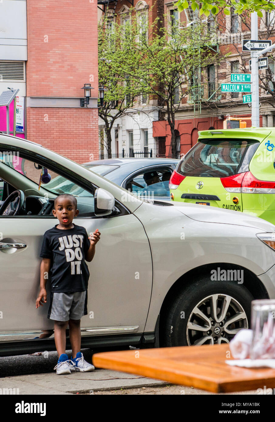 Ragazzo che indossa un 'Just Do It in piedi accanto a AUTO, tirando il viso, Harlem, New York City, Stati Uniti d'America Foto Stock