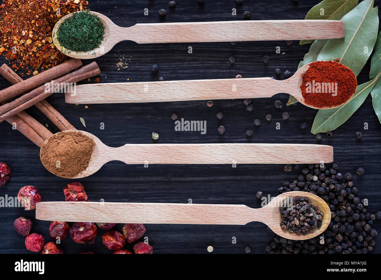 Quattro cucchiai di legno con varie spezie scuro su sfondo di legno Foto Stock
