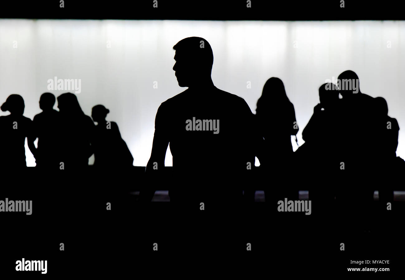 Silhouette di un giovane uomo in piedi da sola e una folla di gente che camminava sfocato dietro di lui nella notte Foto Stock