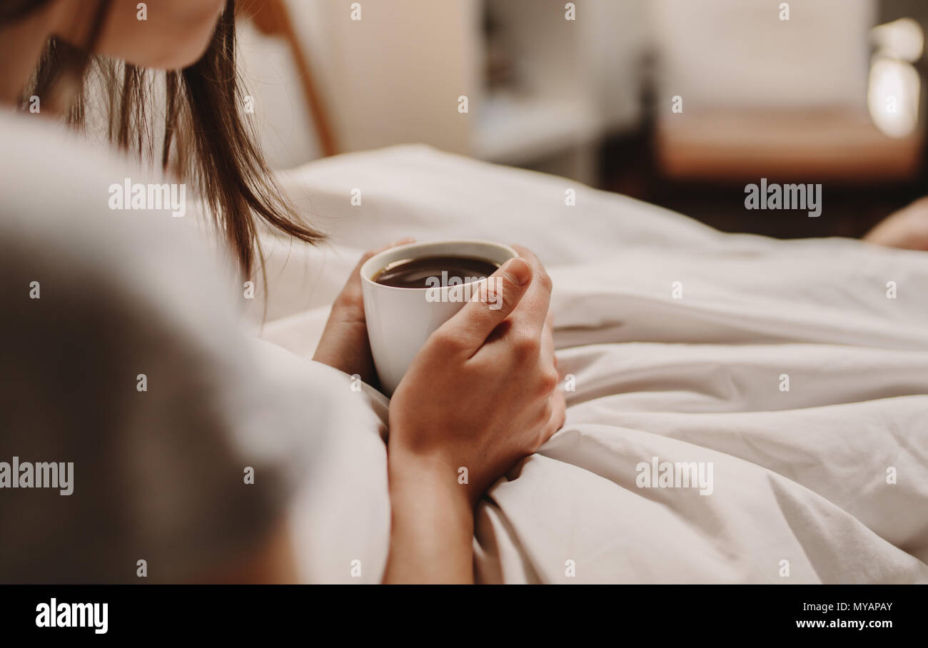 In prossimità di una donna seduta sul letto tenendo una tazza di caffè. Donna con letto caffè in mano seduta sul letto. Foto Stock