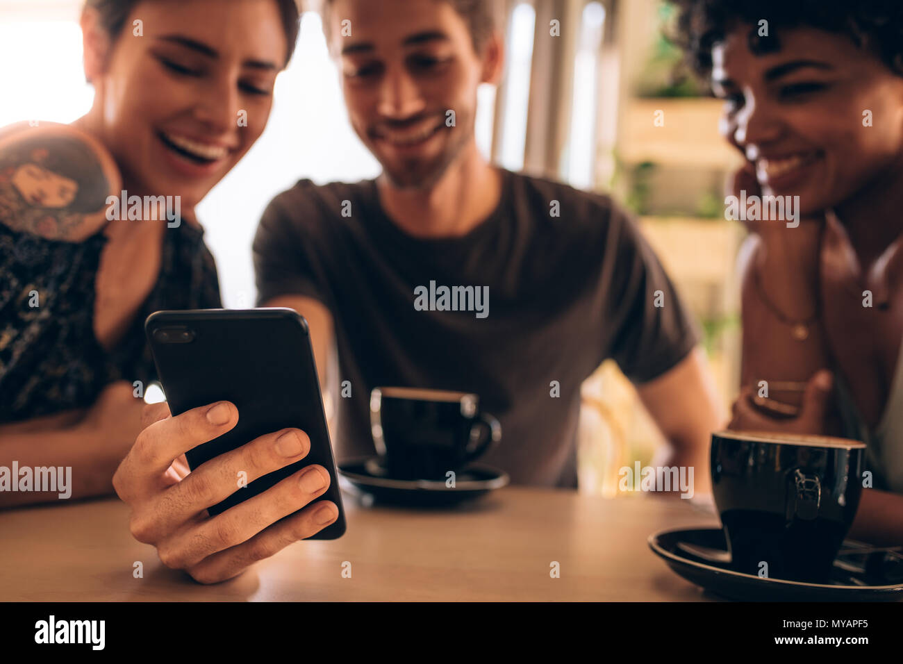 Amici divertendosi utilizzando uno smart phone in cafe. Focus sul telefono cellulare di un uomo con amici di sesso femminile da salotto e sorridente. Foto Stock