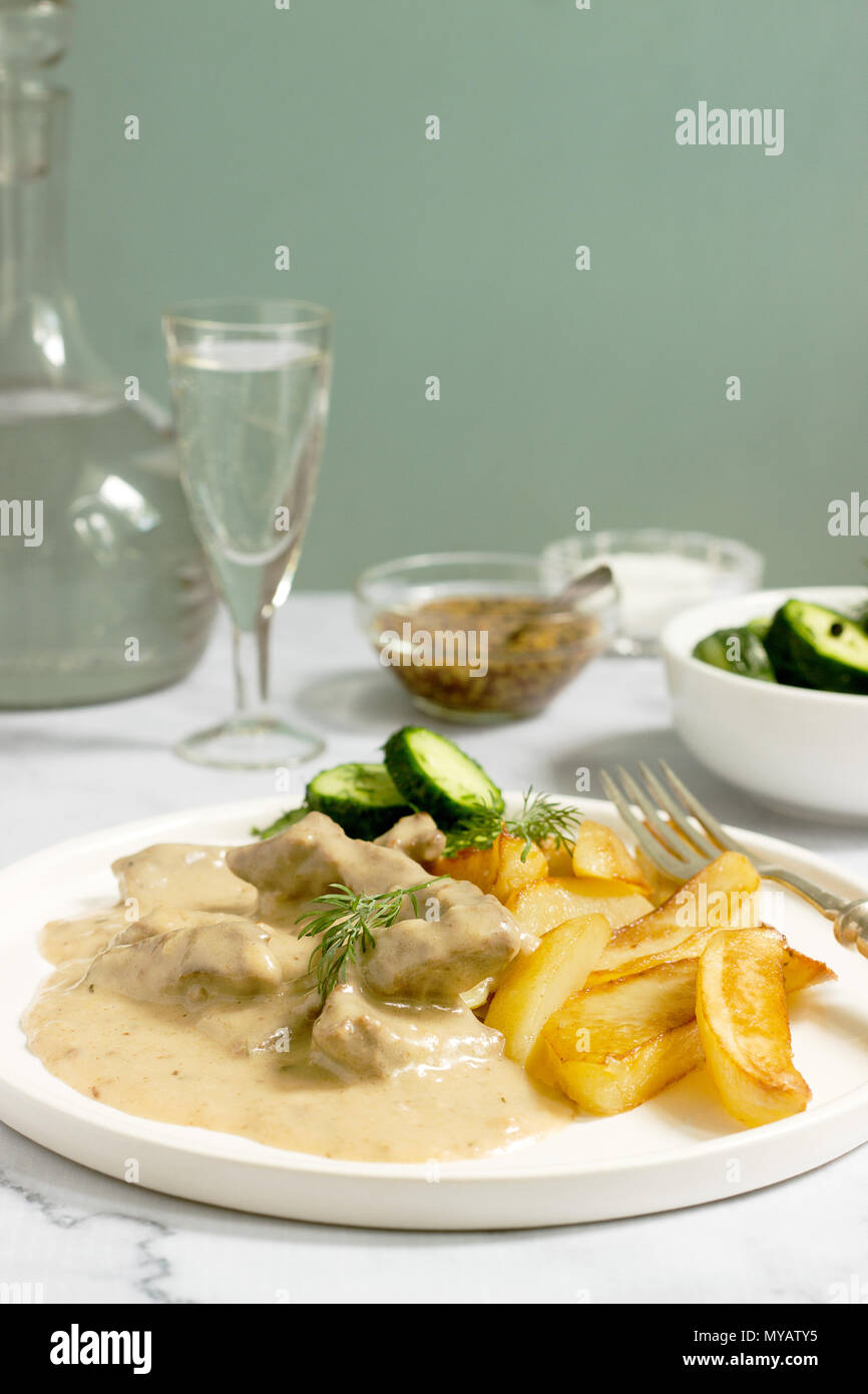 Carni bovine Stroganoff - un tradizionale russo piatto di carni bovine in panna acida salsa, servito con patate fritte, conserve di cetrioli e la vodka. Messa a fuoco selettiva. Foto Stock