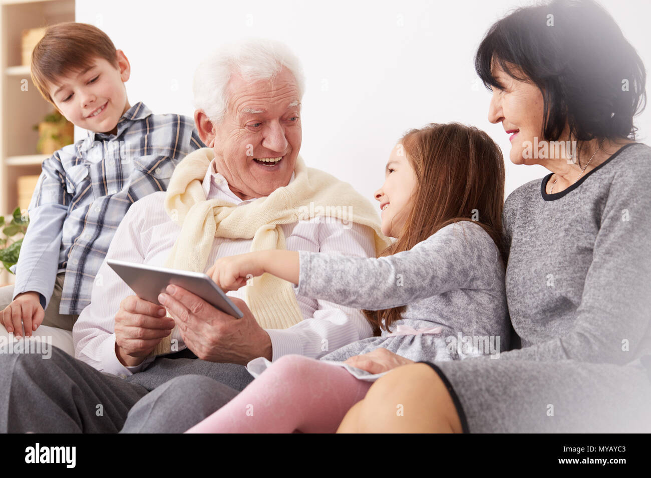 Felice nipoti e nonni utilizzando una compressa in salotto Foto Stock