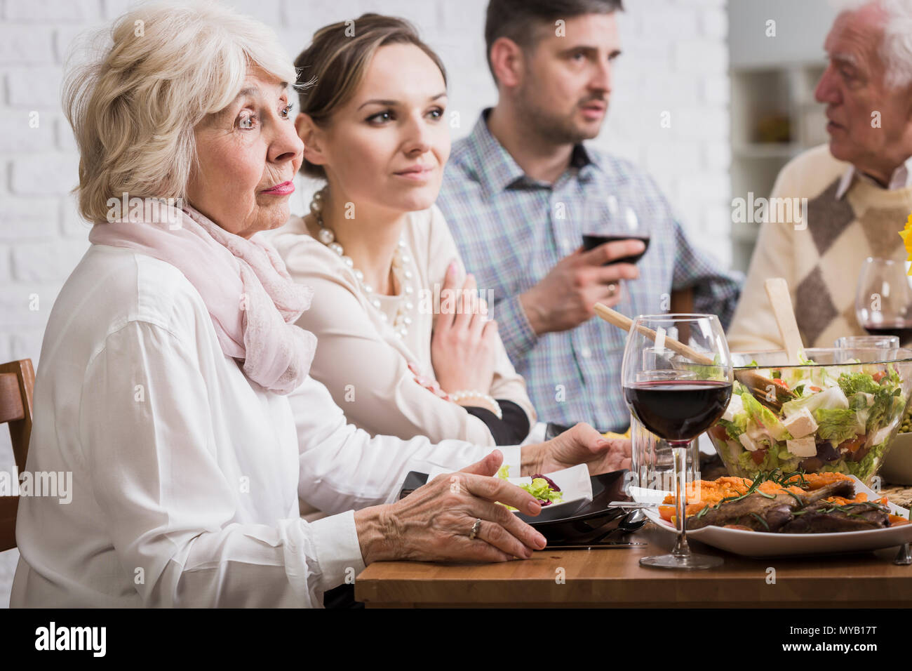 Due uomini e due donne seduto accanto a tavola durante la cena di famiglia, parlando Foto Stock
