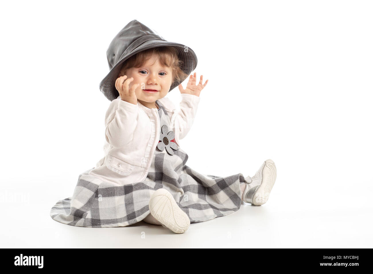 Elegante Happy Baby girl 1 anno vecchio seduto sul pavimento in studio con il nero Cappello in cuoio. Sfondo bianco. Concetto di felicità. Foto Stock