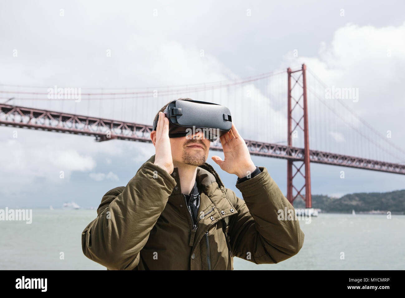 Un uomo utilizza occhiali per realtà virtuale. Il concetto di viaggio virtuale. Xxv Aprile ponte a Lisbona in background. Il concetto moderno di technologie Foto Stock