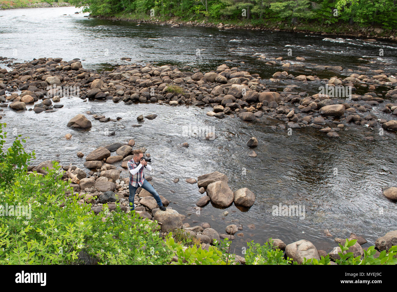 Un fotografo in piedi sulle rocce sul bordo del fiume Hudson vicino al fiume del Nord, NY USA nelle Montagne Adirondack Foto Stock