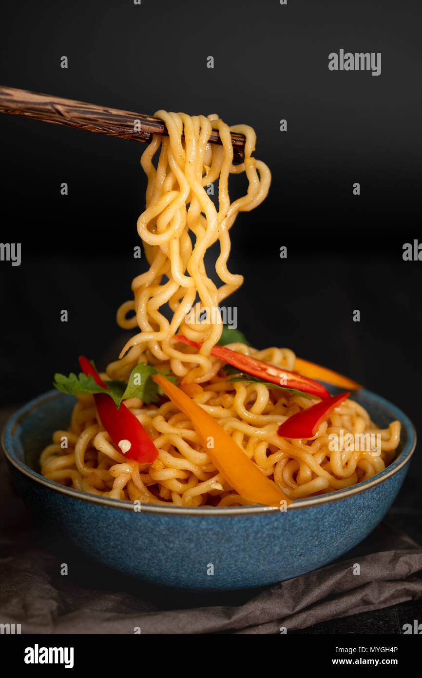Ancora vita spaghetti istantanei con fette di peperone su chopstick, cibo spazzatura o fast food concept. Foto Stock