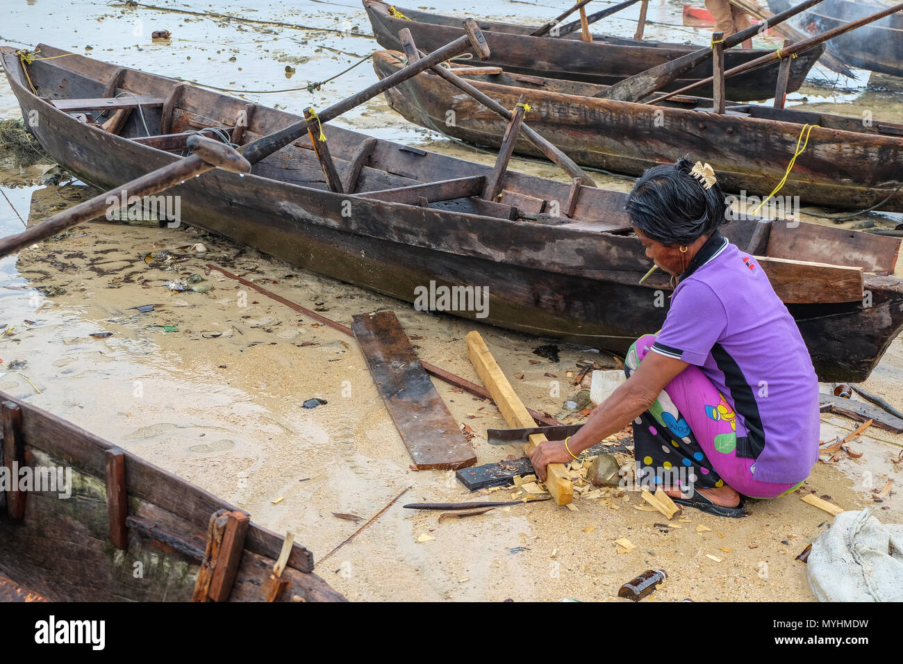 1 maggio 2018 - Arcipelago di Myeik, Myanmar. Moken donna riparazione Canoe sulla spiaggia Foto Stock