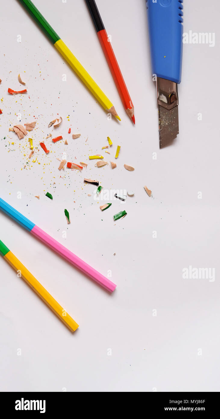 Piatto di laici matite di colore e una blu coltello con matita colorata trucioli sparse su un libro bianco sullo sfondo. Foto Stock
