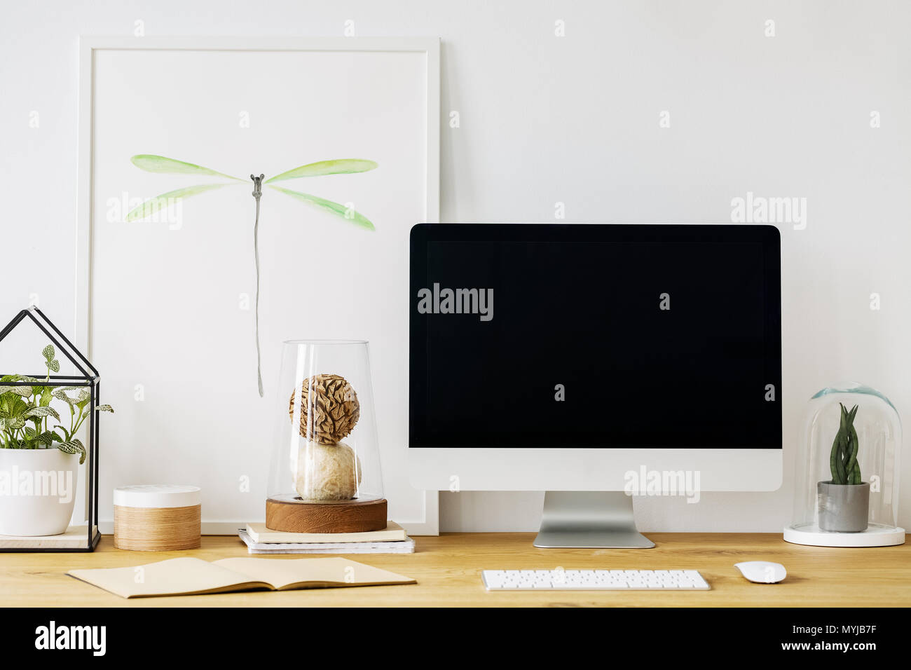 Foto reale di una scrivania con un vuoto di schermo di computer, ornamenti e un poster in una sala interna Foto Stock