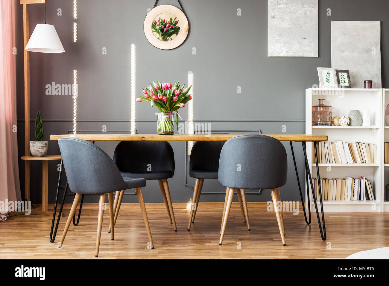 Tavolo da pranzo in legno, sedie grigio, scaffale e tulipani rosa in sala da pranzo interno Foto Stock